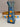A rectangular glass vase with a flared base, decorated with a hand-painted traditional Spanish style pattern of blue leaves and yellow-orange flowers on a white background, mounted on a beige woven basket.